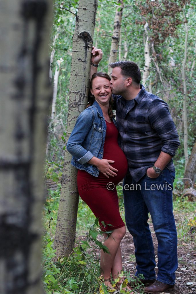 Candid maternity photo of a laughing couple, with the woman in a red maternity dress, in an Edmonton park.