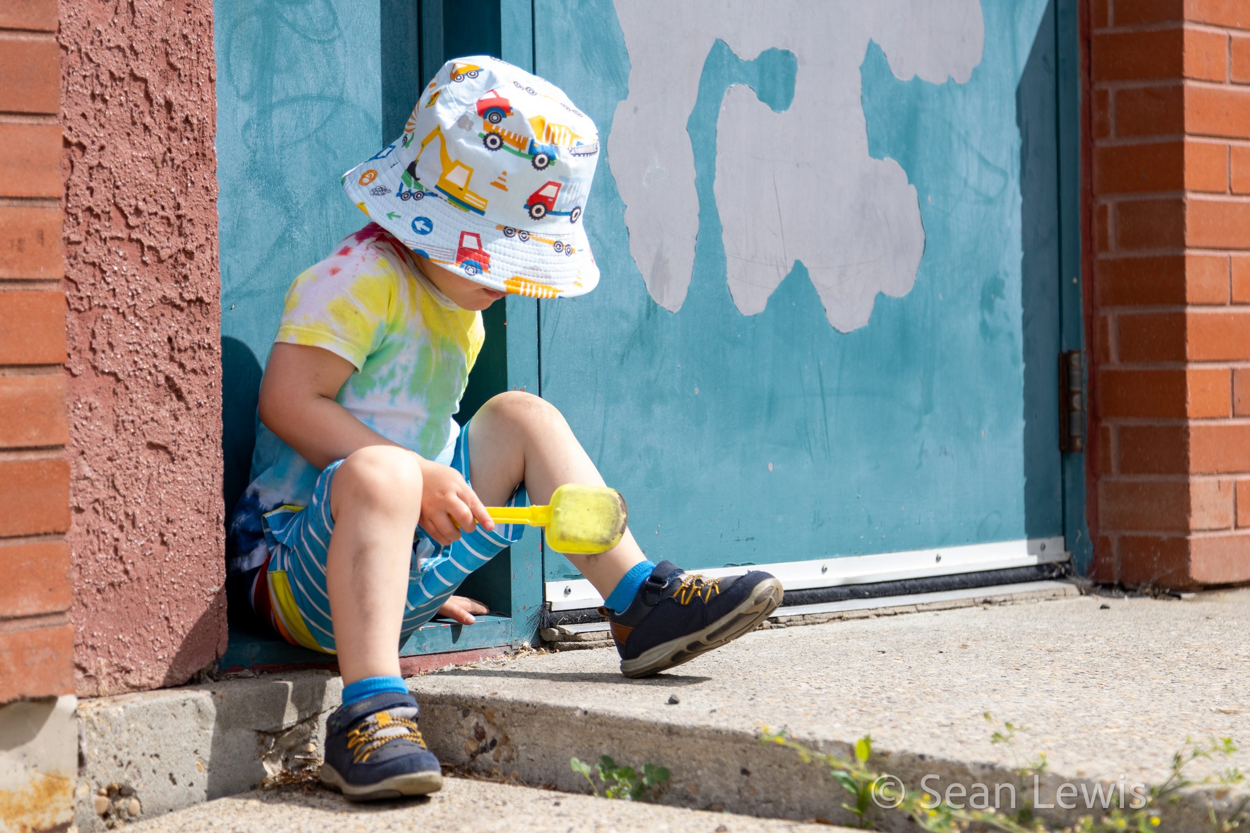 Candid portrait of a child in a colourful hat sitting on steps during an outdoor Edmonton family session.