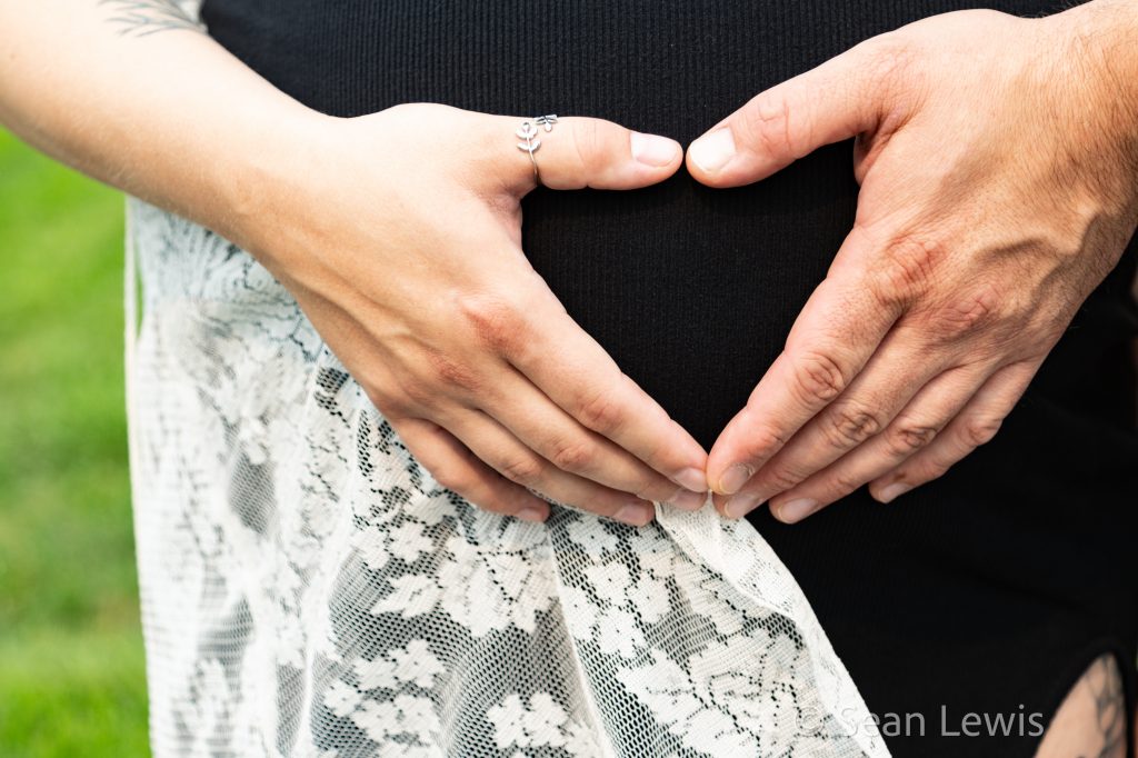 Close-up of hands making a heart on a pregnant belly during an Edmonton maternity photo session.