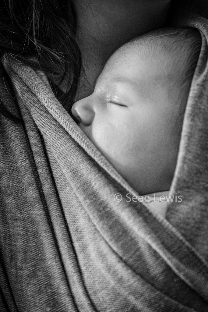 Black and white close-up of a newborn baby sleeping safely in a sling during a Leduc family session.