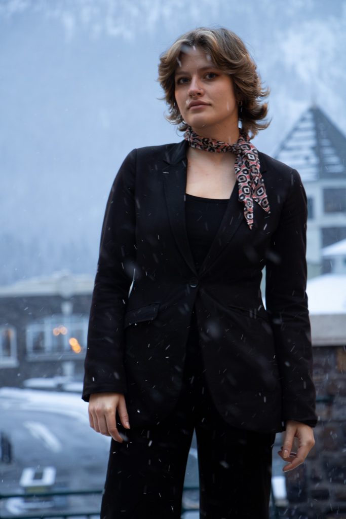 Modern corporate portrait of a woman in a black coat, with Fairmont Banff Springs behind her.