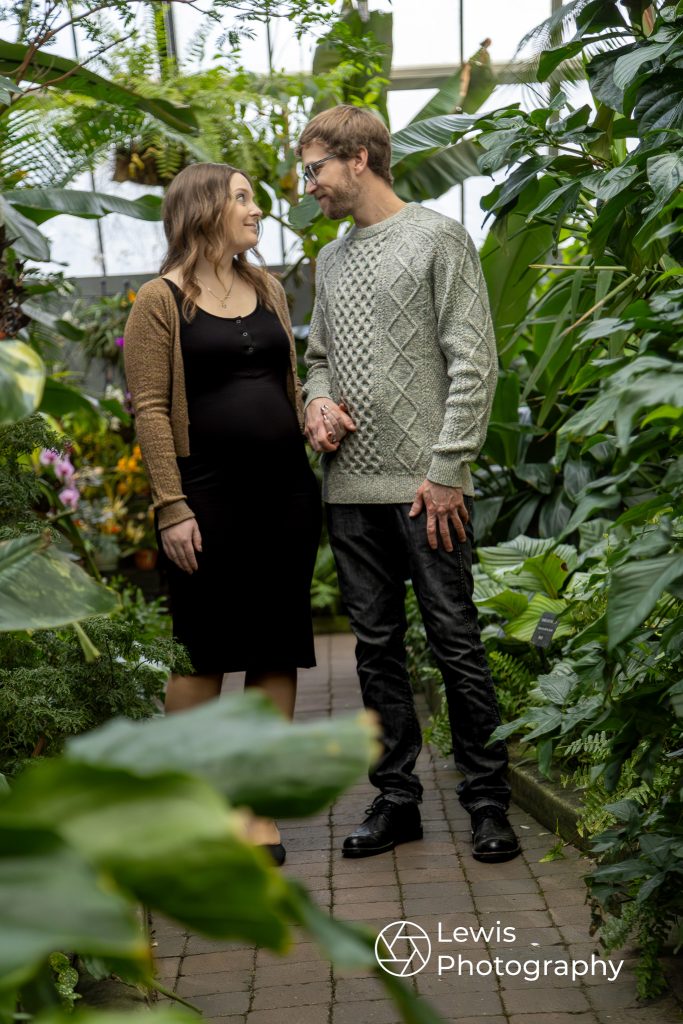Maternity photo of a couple standing together in a lush, green conservatory in Edmonton.