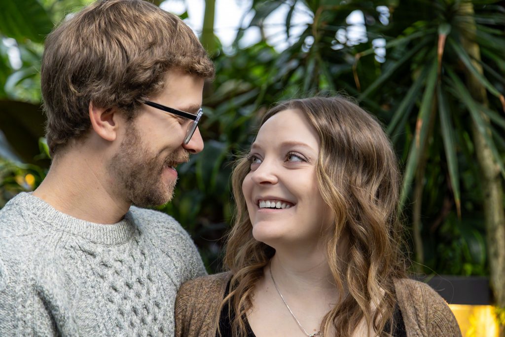 A couple in love share a smile at an Edmonton Muttart Conservatory indoor photo shoot.