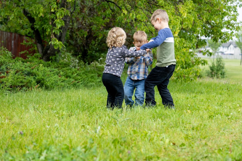 three cute kids playing in the edmonton grass